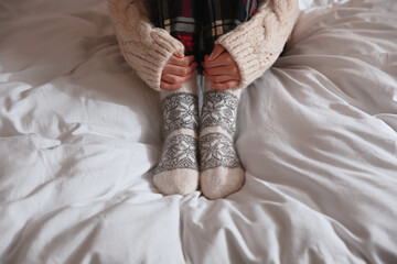 Woman wearing knitted socks on bed with soft blanket, closeup