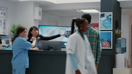 Diverse group of patients asking for help at hospital reception, waiting to attend medical checkup appointment. Sitting in waiting room lobby for healthcare support. Handheld shot.