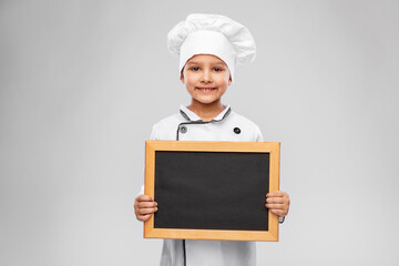 cooking, culinary and profession concept - happy smiling little girl in chef's toque and jacket holding chalkboard over grey background