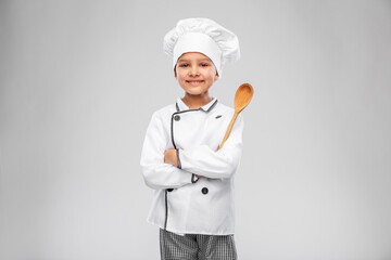 cooking, culinary and profession concept - happy smiling little girl in chef's toque and jacket with wooden spoon over grey background