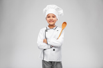cooking, culinary and profession concept - happy smiling little girl in chef's toque and jacket with wooden spoon over grey background