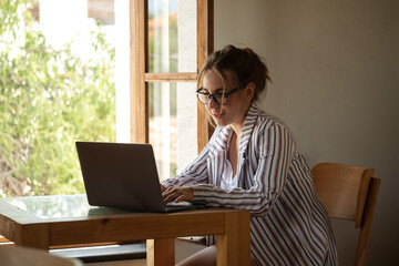 Happy young businesswoman sitting at table with laptop next to window. Skilled manager saleswoman calling customer, giving professional consultation.