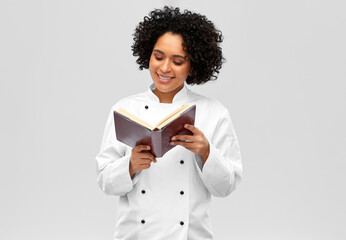 Fototapeta premium cooking, culinary and people concept - happy smiling female chef reading cook book over white background