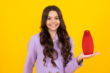 Teen child girl with shampoo bottle or shower gel isolated on yellow background. Kids hair cosmetic product. Happy teenager, positive and smiling emotions of teen girl.