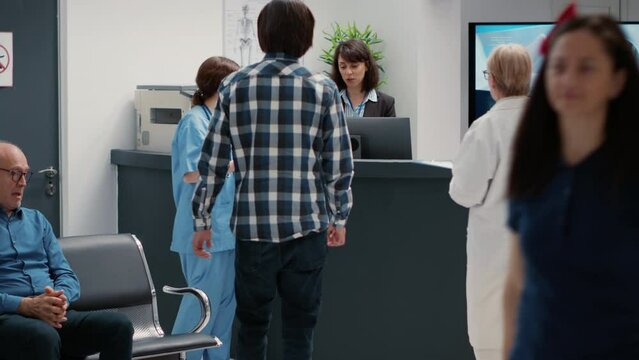 Busy reception desk with many patients waiting to attend consultation, trying to write medical report in hospital lobby. Diverse people having appointments in waiting room area.