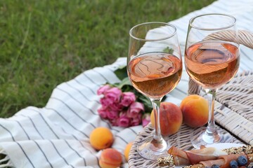 Glasses of delicious rose wine, food, flowers and basket on picnic blanket outdoors