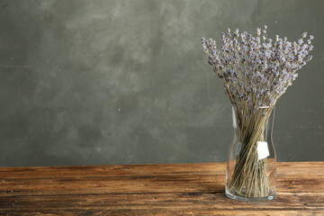 Dried lavender flowers in glass vase on wooden table against grey background. Space for text