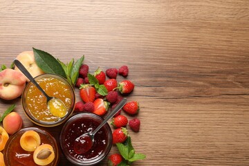 Jars with different jams and fresh fruits on wooden table, flat lay. Space for text