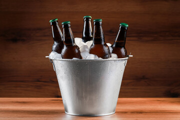 Metal bucket with bottles of beer and ice cubes on wooden table