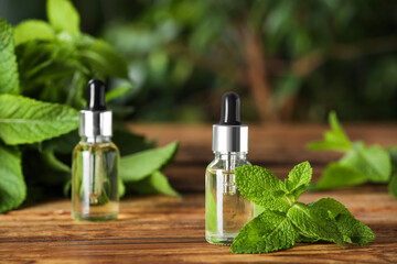 Bottles of mint essential oil and green leaves on wooden table