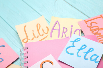 Paper notes with different baby names and notebook on light blue wooden table, closeup