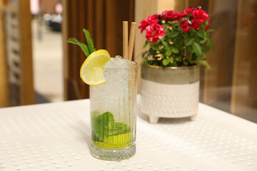 Glass of refreshing citrus drink and potted flowers on white table indoors