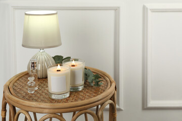 Burning soy candles, lamp, perfumes and eucalyptus branch on wicker table indoors. Space for text