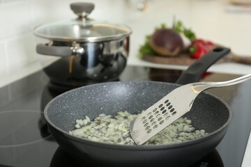 Frying chopped onion on cooktop in kitchen, closeup