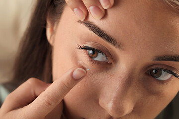Young woman putting contact lens in her eye on blurred background, closeup