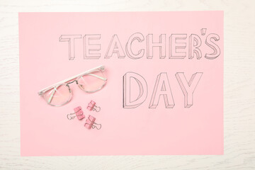 Fototapeta na wymiar Sheet of pink paper with words TEACHER'S DAY, glasses and clips on white wooden background, top view