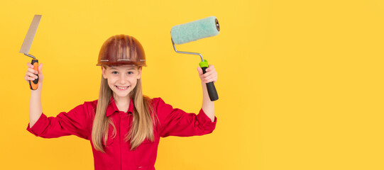 glad teen child in builder hard hat with paint roller and spatula on yellow wall. Child builder in helmet horizontal poster design. Banner header, copy space.