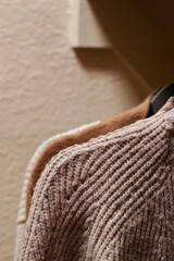 Fototapeta na wymiar close up of pastel warm knitted cardigan sweater hanging in the closet. Cozy fall and winter wardrobe.