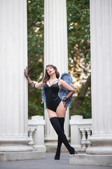 Beautiful girl with red lips in a black bodysuit, gloves and blue wings. Posing, leaning on a column
