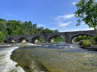 Fototapeta na wymiar Five-span stone bridge in Pakenham, Ontario with rapids in the foreground and forested shores