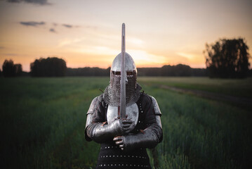 The knight in the plate armor and helmet holds a sword in hands close up.