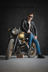 A motorcyclist in the black leather jacket and sunglasses on the old motorbike.