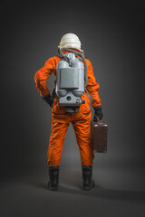 Astronaut in the space suit and helmet is standing with the travel suitcase in hand on the gray...