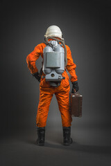 Astronaut in the space suit and helmet is standing with the travel suitcase in hand on the gray background. Space tourism concept. © Dmitriy