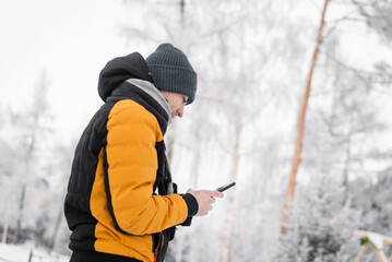 Young man in the winter park with a mobile phone in the hand portrait.