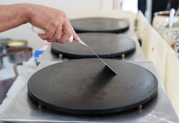 preparando a chapa para fazer crepe durante a festa. Raspando a chapa quente com a espatula