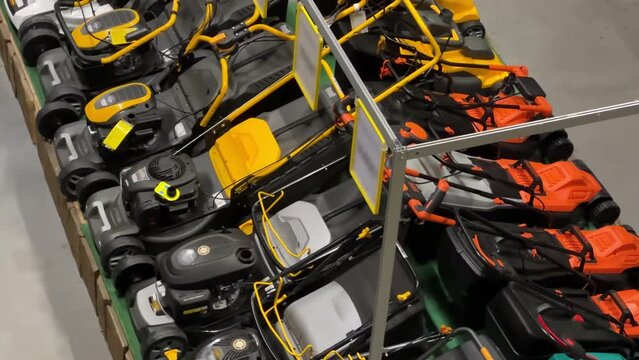 Rows of electric and gasoline lawn mowers stand in a home and garden store. Top view