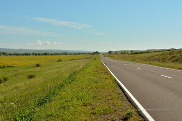 Fototapeta na wymiar A straight asphalt road going through the endless hilly steppe on a warm summer day.