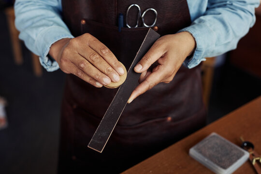 Close up unrecognizable artisan shaving leather piece in leatherworking shop, copy space