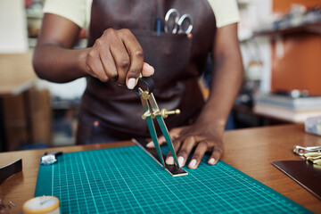 Close up of black female artisan measuring leather piece in leatherworking shop, copy space