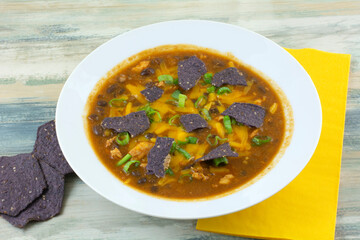 Chicken and black bean soup with blue corn tortilla chips in white bowl with yellow napkin