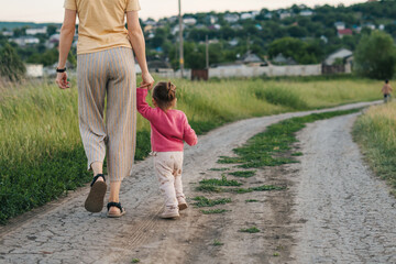Back view of a mother and daughter walking happy at sunset, holding their hands. Parent, child. Happy family, childhood. Summer nature. Mother nature.