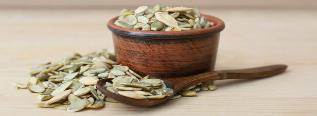 Bowl and spoon with healthy pumpkin seeds on light table