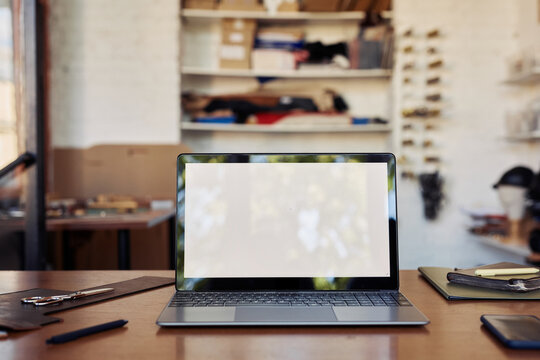 Background image of opened laptop with blank screem nock up on table in workshop interior, copy space