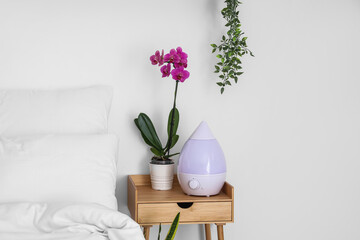 Orchid flower and humidifier on bedside table near white wall