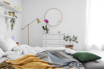 Comfortable bed, chest of drawers and houseplants near white wall in bedroom interior