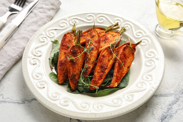Plate of tasty baked carrots with greens on table, closeup