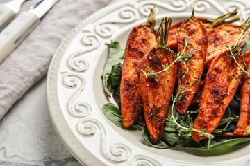 Plate of tasty baked carrots with greens on table, closeup