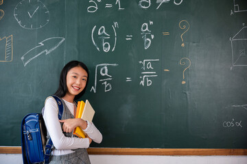 Back to school. Happy beautiful Asian Schoolgirl girl standing holding books standing in front blackboard of classroom, Portrait of smiling woman child student of black chalk board, Education lesson - obrazy, fototapety, plakaty