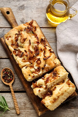 Board with tasty Italian focaccia, jug of oil and peppercorns on wooden background, closeup