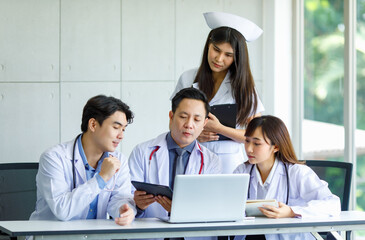 Group of Asian successful professional male and female doctors in white lab coat uniform with stethoscope and nurse sitting meeting discussing together holding human skeleton model in hospital office