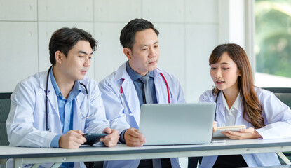 Group of Asian successful professional male and female doctors in white lab coat uniform with stethoscope sitting meeting together using laptop notebook computer and tablet working researching online