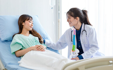 Obraz premium Asian young professional female doctor in white lab coat with stethoscope sitting holding human spine skeleton model showing explaining supporting comforting patient laying down on bed in ward room