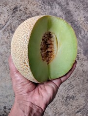 A man's left hand holds a partially cut melon 
