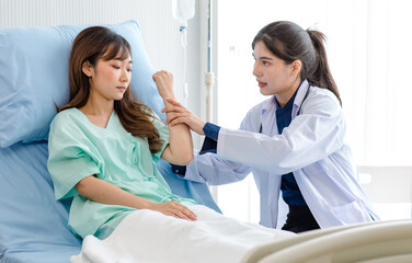 Asian young professional female practitioner doctor in white lab coat with stethoscope holding touching checking monitoring patient injury arm and muscle while laying down on bed in hospital wardroom
