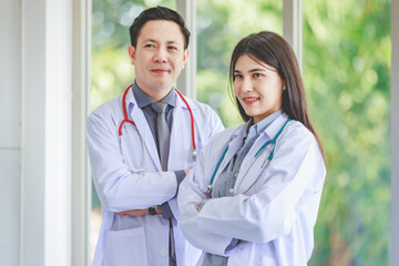 Asian young cheerful professional male and female intern practitioner doctor colleague in white lab coat uniform with stethoscope standing smiling together holding patient paperwork document folder